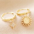 Close Up of Sunburst and Star Charm Huggie Hoop Earrings in Gold on Beige Fabric