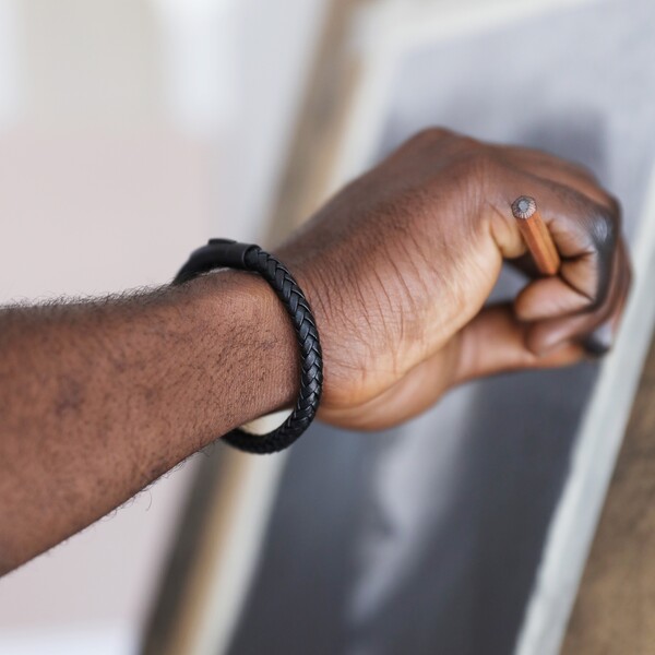 Men's Personalised Leather Bracelet with Matte Black Clasp on model holding hand up to painting