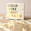 30 Battery Powered LED Gold Wire String Lights and packaging on wooden table