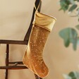 Large Starry Gold Velvet Christmas Stocking Hanging from Wooden Chair Next to Plant