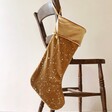Large Starry Gold Velvet Christmas Stocking on Wooden Chair in Empty Room