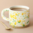 Sass & Belle Yellow and Green Splatterware Mug Filled With Hot Drink on Neutral Background
