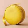 Front of Mini Round Travel Jewellery Case in Mustard on Pink Background