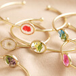 Collection of Pressed Birth Flower Bangles in Gold Layered on Top of Each Other with Neutral Background