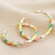 Close Up of Multicolour Enamel Rope Hoop Earrings in Gold on Beige Fabric