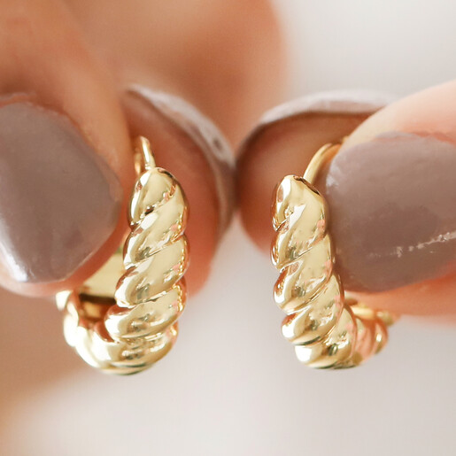 Model Holding Small Chunky Rope Huggie Hoop Earrings in Gold in Gold Against a Cream Backdrop