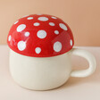 Sass & Belle Red Mushroom Mug with Lid Against Neutral Background