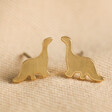 Brushed Dinosaur Stud Earrings in Gold Against Natural Coloured Fabric
