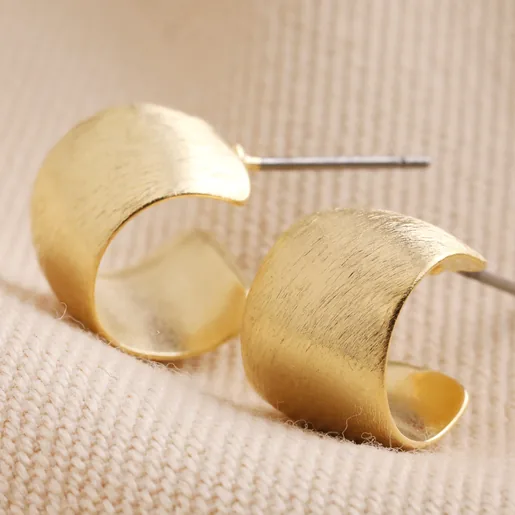 Brushed Wide Gold Huggie Hoop Earrings in Gold on Beige Fabric
