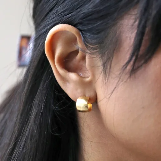 Model Wearing Brushed Wide Gold Huggie Hoop Earrings in Gold Close Up
