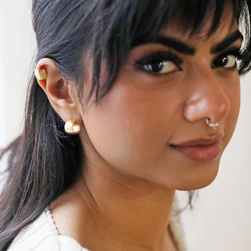 Model Looking into Camera Wearing Brushed Wide Gold Huggie Hoop Earrings in Gold with Matching Ear Cuff