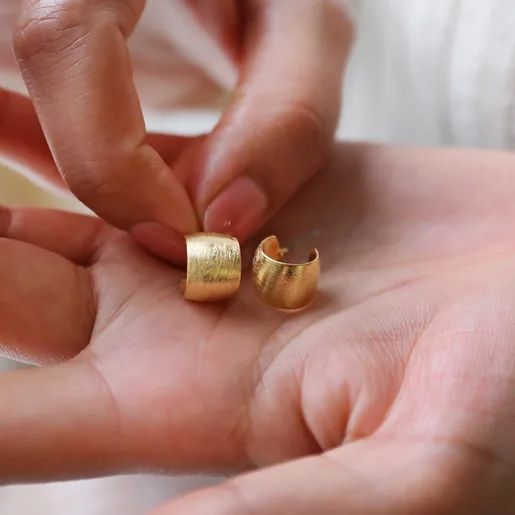 Model Holding Brushed Wide Gold Huggie Hoop Earrings in Gold in Palm of Hand