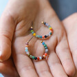 Model Holding Colourful Small Beaded Hoop Earrings in Gold