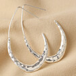Hammered Teardrop Hoop Earrings in Silver on Beige Coloured Fabric 