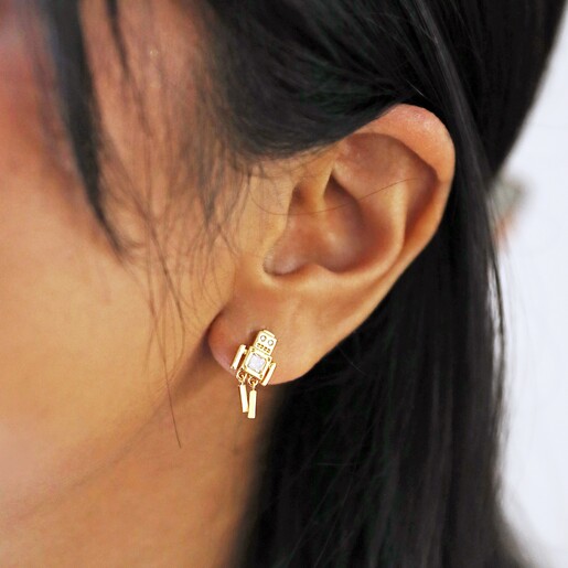 Close Up of Mismatched Robot and Star Stud Earrings in Gold on Model with Neutral Background