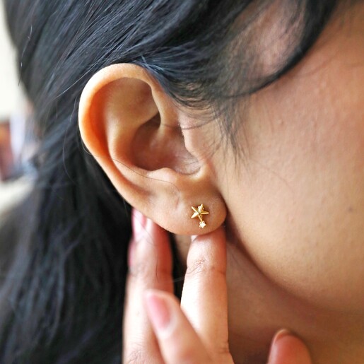 Close Up of Star Stud from Mismatched Robot and Star Stud Earrings in Gold on Model Hand on Ear