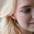 Close Up of Blonde Model Wearing Small Gold Flower and Green Crystal Drop Earrings