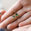 Model Holding Small Gold Flower and Green Crystal Drop Earrings Between Fingers