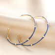 Blue Enamel Bamboo Style Hoop Earrings in Gold on top of beige coloured fabric