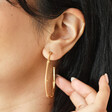 Close up of Brown Enamel Bamboo Style Hoop Earrings in Gold on model with hand behind ear