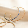Blue Enamel Bamboo Style Hoop Earrings in Gold with brown version on top of beige coloured material