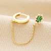 Green Crystal Stud Huggie and Chain Earring in Gold laid on top of neutral coloured fabric