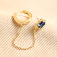 Blue Crystal Stud Huggie and Chain Earring in Gold laid on top of neutral coloured fabric