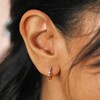 Close up of Pastel Baguette Crystal Huggie Hoop Earrings in Gold on model