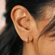 Close up of Pastel Baguette Crystal Huggie Hoop Earrings in Gold on model