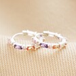 Pastel Baguette Crystal Huggie Hoop Earrings in Silver laid out on neutral coloured fabric