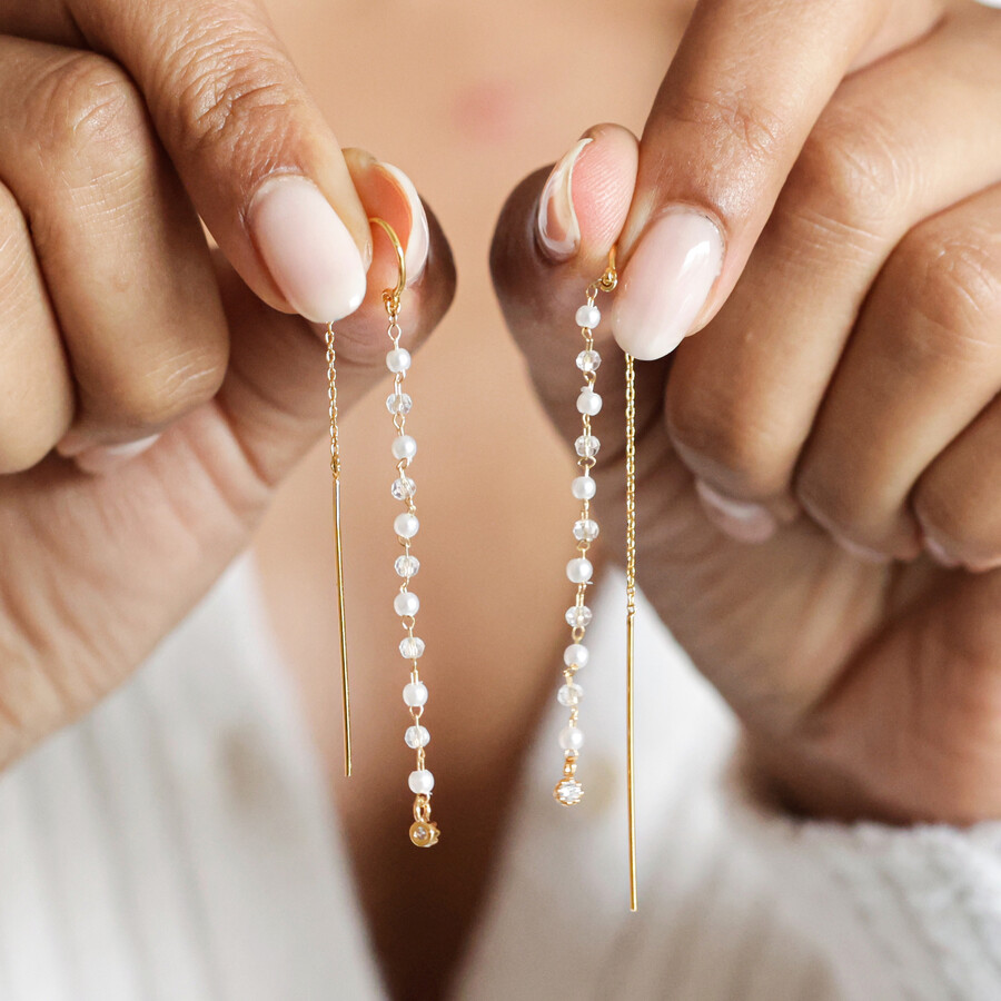 Model holding Thread Through Crystal and Pearl Chain Earrings in Gold