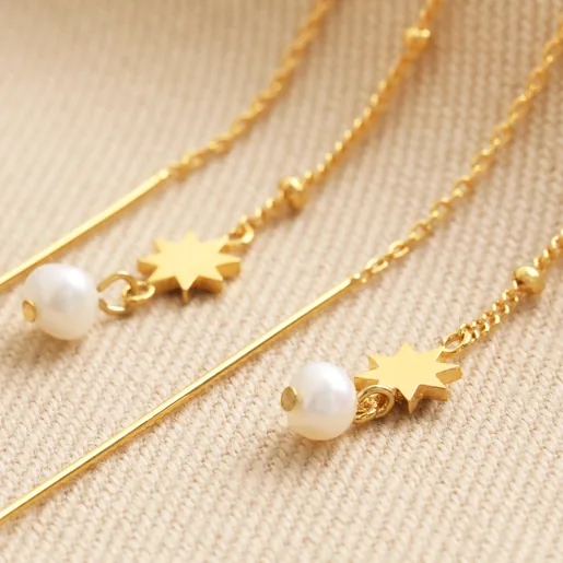 Close Up of Thread Through Star and Pearl Chain Earrings in Gold on Beige Fabric