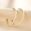 White Enamel Twisted Hoop Earrings in Gold on Beige Fabric