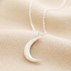 Crescent Moon Pendant Necklace in Silver laid out on top of beige coloured surface