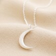 Crescent Moon Pendant Necklace in Silver laid out on top of beige coloured surface