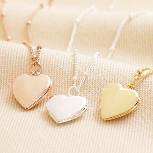 Also Available in Silver and Rose Gold Heart Locket Necklace in Gold with rose gold and silver necklaces against beige backdrop