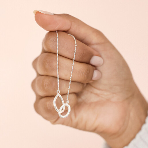 Model holding Organic Interlocking Hoops Necklace in Silver in front of neutral backdrop