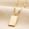 Tiny Hammered Tag Pendant Necklace in Gold on top of neutral coloured fabric