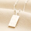 Tiny Hammered Tag Pendant Necklace in Silver on top of beige coloured fabric