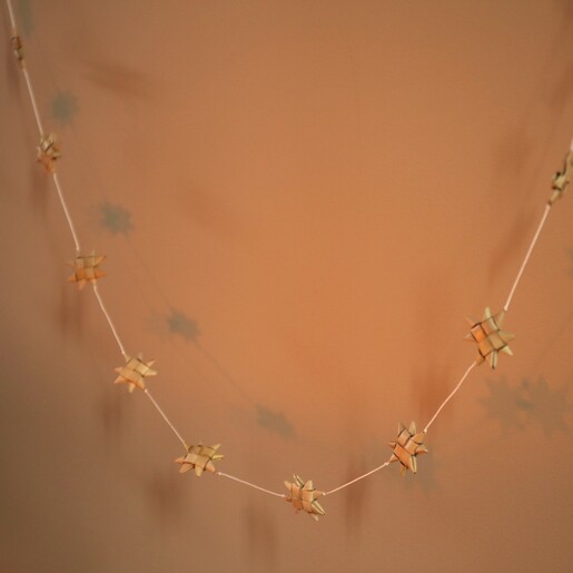 Afroart Natural Stars on a String Garland in warm lighting in front of neutral wall 