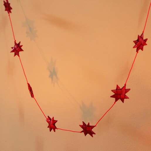 Afroart Red Stars on a String Garland hanging in front of neutral background in warm lighting