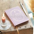 Pink Sun and Moon Fabric Notebook on top of wooden counter with candle and pencil next to it