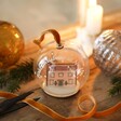 Personalised Festive House Glass Dome Bauble on wooden surface surrounded by Christmas decorations