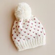 Hat from White and Pink Knitted Bobble Hat and Mittens Set on Beige Background