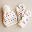 White and Pink Knitted Bobble Hat and Mittens Set on Beige Background