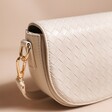 Close up of gold hardware on Woven Vegan Leather Crossbody Bag in Beige in front of neutral coloured backdrop