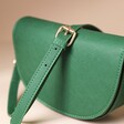 Vegan Leather Half Moon Crossbody Bag in Green with Strap Draped Over Top on Beige Background 