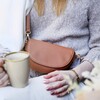Close Up of Vegan Leather Half Moon Crossbody Bag in Tan on Model Drinking Coffee