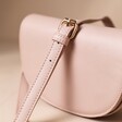 Vegan Leather Half Moon Crossbody Bag in Pink with Strap Draped over the Top on Beige Surface