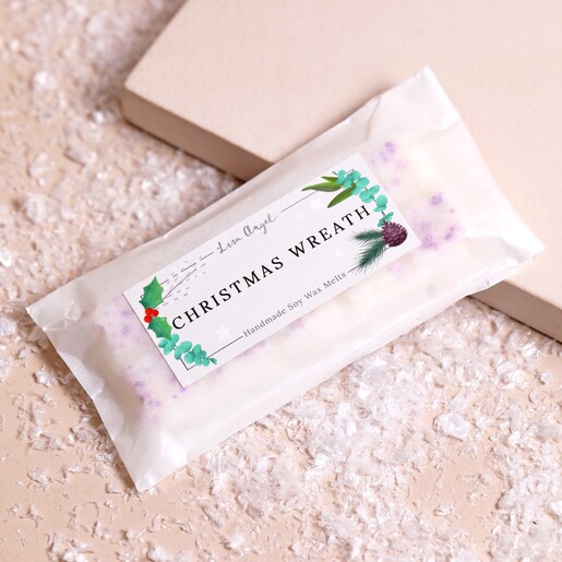 Lisa Angel Christmas Wreath Soy Wax Melts in packaging on top of beige coloured backdrop with fake snow